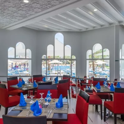 Restaurant panoramique vue piscine avec chaises rouges et serviettes bleues au Marhaba Palace à Monastir.