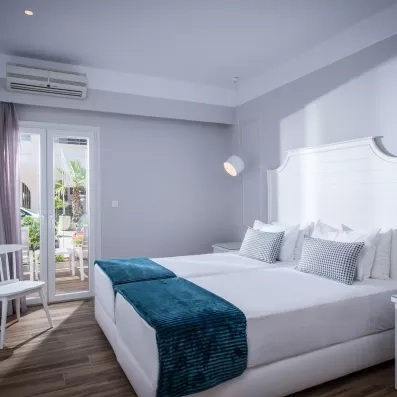 chambre avec 2 lits collés et grande tête de lit en blanc une porte fenêtre, et un climatiseur 