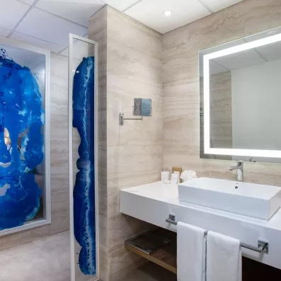 salle de bains avec douche et sèche-cheveux, grand miroir avec de la lumière, vasque carrée, petit miroir grossissant