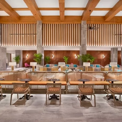 salon proche de l'accueil, banquettes et chaises en osier, plantes, lampes sur les tables