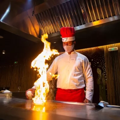 cuisinier faisant flamber un plat, toque et tablier rouges et blouse blanche, démonstration de show cooking