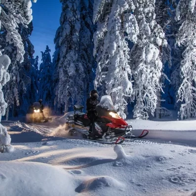 Safari nocturne en motoneige à travers les sapins chargés de neige au Samperin Savotta, Finlande.