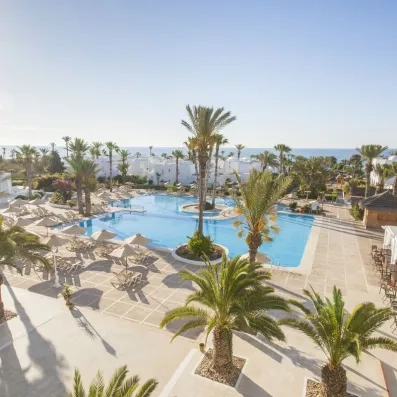 Terrasse ensoleillée du Seabel Aladin avec chaises longues, parasols et vue dégagée sur la piscine et la mer en arrière-plan.