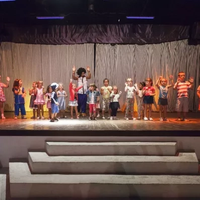 Enfants participant à un spectacle sur scène avec animateur dans une ambiance festive.