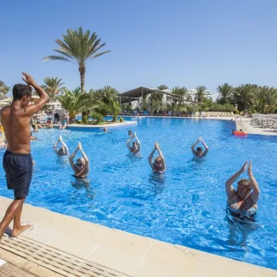 Cours d’aquagym dans une piscine extérieure avec instructeur et palmiers en arrière‑plan.