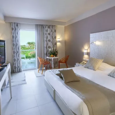 Chambre d’hôtel moderne avec lit double, décoration élégante et balcon offrant une vue sur les palmiers.