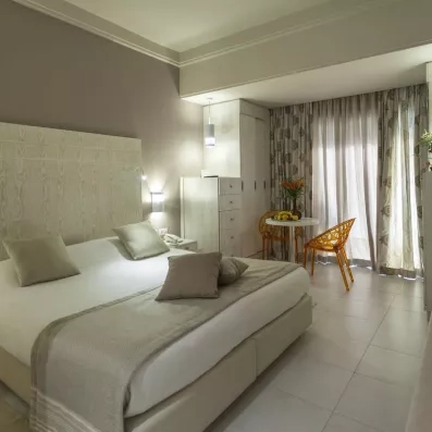 Chambre d’hôtel chaleureuse avec lit double, mobilier en bois clair et coin salon en rotin.”