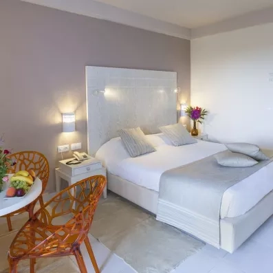 Chambre d’hôtel élégante avec lit double, lampes murales et coin détente avec fleurs et fruits.