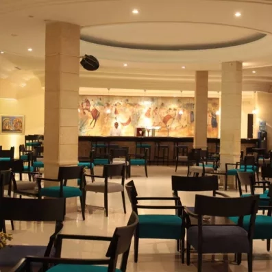 Lounge moderne avec chaises noires, bar éclairé et fresque colorée représentant une scène désertique.