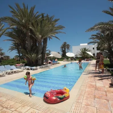 Piscine extérieure familiale avec palmiers, transats, parasols et enfant sortant de l’eau