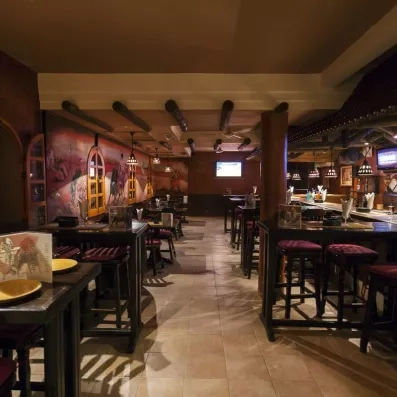 “Bar chaleureux avec tables hautes, fresques colorées, éclairage tamisé et ambiance conviviale