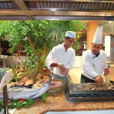 Chefs en cuisine préparant du poisson frais avec herbes, légumes et grande pièce de poisson exposée