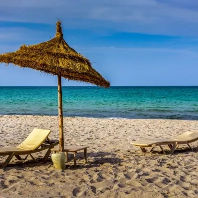 Plage de sable fin et parasol typique à Djerba pour une journée détente en formule tout inclus.