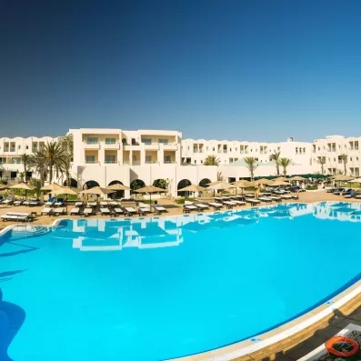 Grande piscine extérieure de l'hôtel Ulysse Djerba bordée de transats sous un ciel bleu azur éclatant.