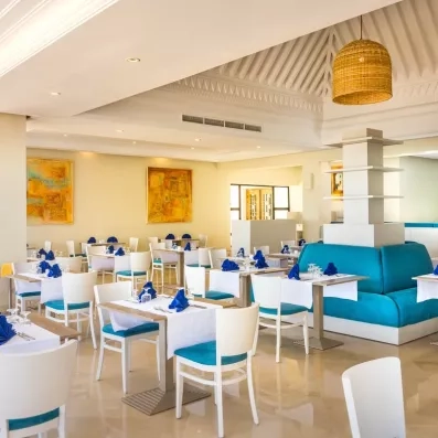 Salle de restaurant lumineuse de l'hôtel Ulysse Djerba avec décoration moderne et chaises bleu turquoise.