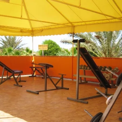 Salle de sport extérieure ombragée avec équipements de musculation au complexe hôtelier Vincci Dar Midoun.
