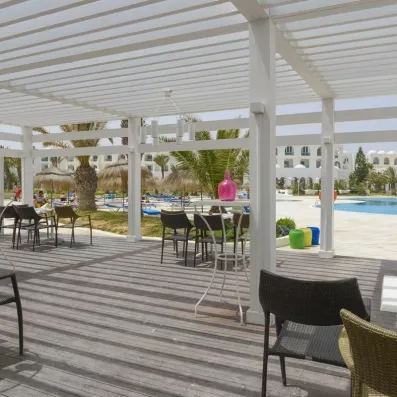 Terrasse ombragée sous une pergola blanche offrant une vue imprenable sur la piscine de l'hôtel à Djerba.