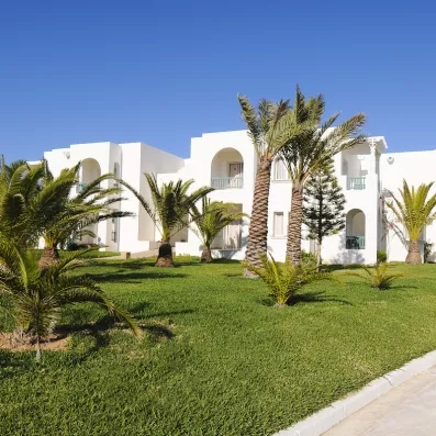 Architecture traditionnelle tunisienne et palmiers exotiques dans les jardins ensoleillés de l'hôtel Helios Beach à Djerba.