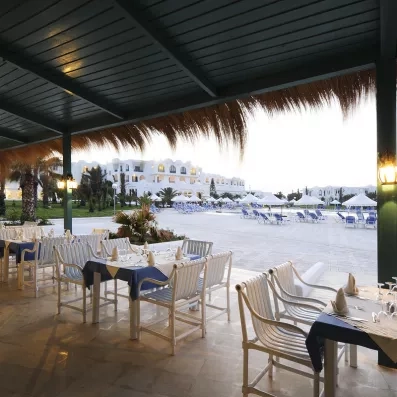 Terrasse du restaurant extérieur de l'hôtel Helios Beach avec vue sur la piscine et les jardins exotiques.
