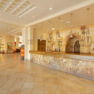 Réception de l'hôtel Safira Palms à Djerba avec un comptoir en bois et une fresque murale traditionnelle.