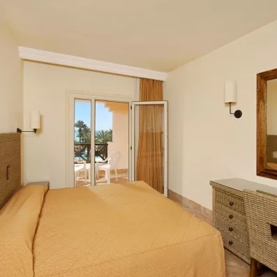 Chambre double confortable avec mobilier en rotin et balcon privé offrant une vue sur mer à Djerba.