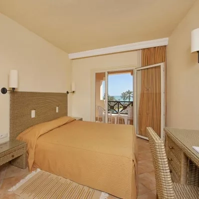 Intérieur de chambre spacieuse au Safira Palms avec bureau, tête de lit tressée et ouverture sur terrasse.