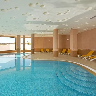 Piscine intérieure chauffée avec transats jaunes et grandes baies vitrées lumineuses à l'hôtel Safira Palms.