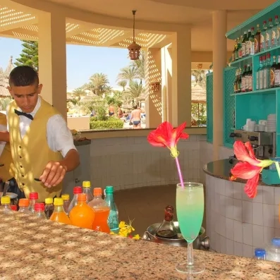 Barman préparant un cocktail coloré au bar de la piscine de l'hôtel Zephir à Djerba.