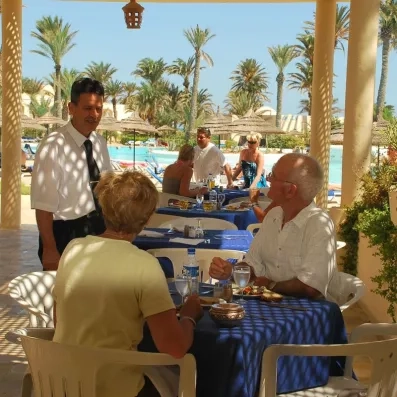 Clients déjeunant en terrasse ombragée face à la piscine et aux palmiers de l'hôtel Zephir.