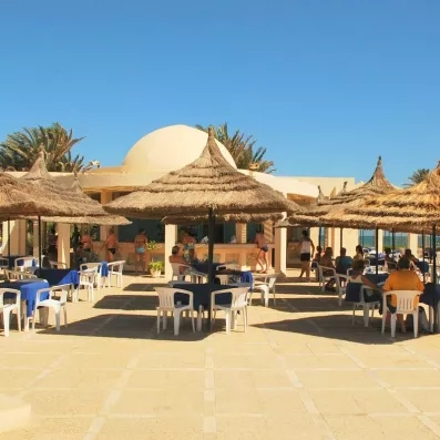 Restaurant de plage extérieur avec parasols en paille et dôme blanc typique de l'architecture de Djerba.