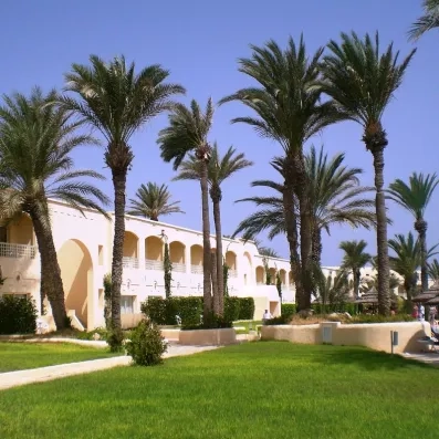 Façade blanche de l'hôtel Zephir nichée dans un jardin luxuriant parsemé de palmiers à Djerba.