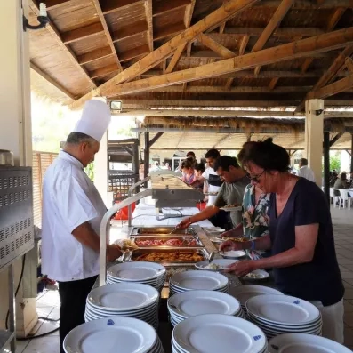 Chef cuisinier servant les clients au buffet de l'hôtel sous une pergola en bois, proposant une variété de plats chauds et spécialités locales.