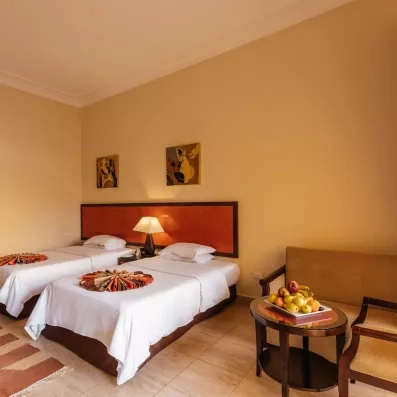 chambre double lits séparés avec canapé beige, table basse, corbeille de fruit