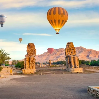 Colosses de Memnon survolés par des montgolfières à l'aube, excursion touristique emblématique en Haute-Égypte.