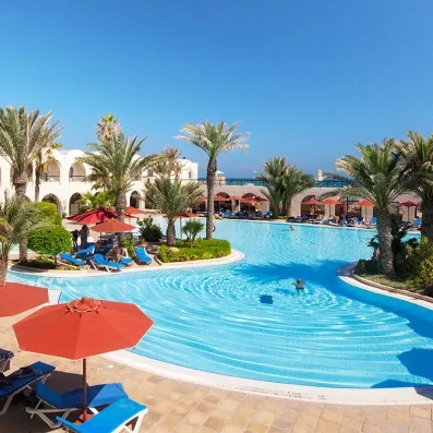 Grande piscine lagon avec parasols rouges et palmiers pour un séjour détente au Sentido Djerba Beach.