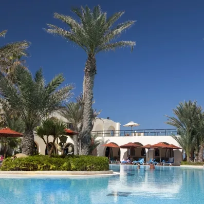 Bassin bleu cristallin entouré de jardins tropicaux et d'architectures blanches typiques de l'île de Djerba.