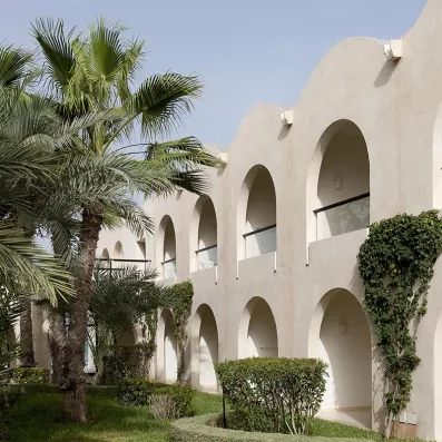 Façade méditerranéenne avec balcons en arcades et végétation luxuriante au cœur du complexe hôtelier Sentido.