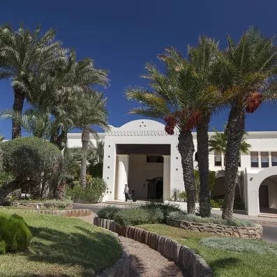 Entrée principale de l'hôtel Sentido Djerba Beach bordée de palmiers sous un ciel bleu azur.