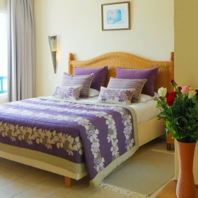 Détail d'un lit double élégant au Djerba Resort avec tête de lit en osier et fleurs fraîches.