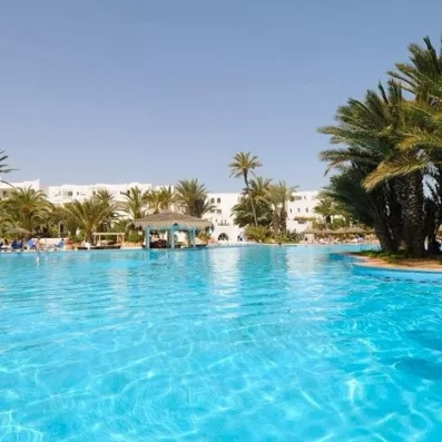 Grande piscine bleue scintillante du Djerba Resort bordée de palmiers sous un ciel d'été radieux.