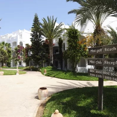 Allée fleurie et panneaux de signalisation vers la plage et le mini-golf au sein du Djerba Resort.
