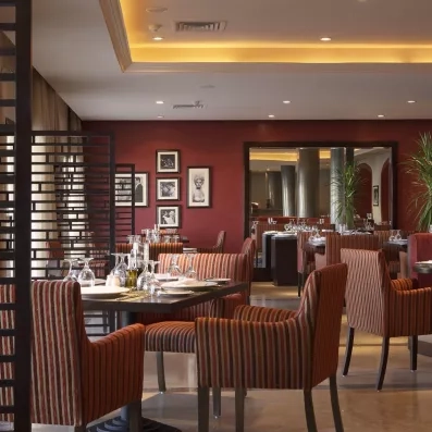 Restaurant chic Jaz Aquamarine Hurghada, dîner gastronomique en Égypte, fauteuils rayés et décoration murale élégante.