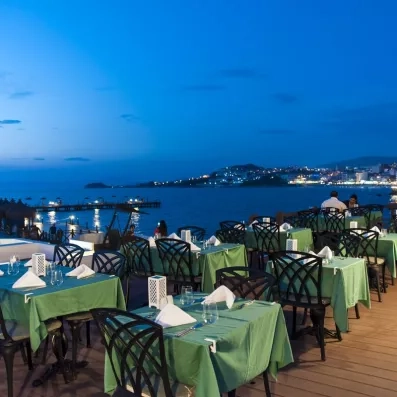 Une terrasse extérieure en soirée avec des tables nappées et vue sur la baie illuminée.
