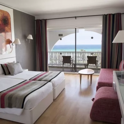 Chambre spacieuse avec balcon vue mer au Mondi Club One Resort Jockey Monastir, Tunisie, dotée de lits twin et d'un coin salon pour des vacances en famille.