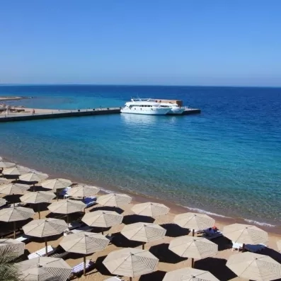 Vue panoramique sur la plage privée, parasols en paille et bateaux de croisière à Hurghada, Égypte.