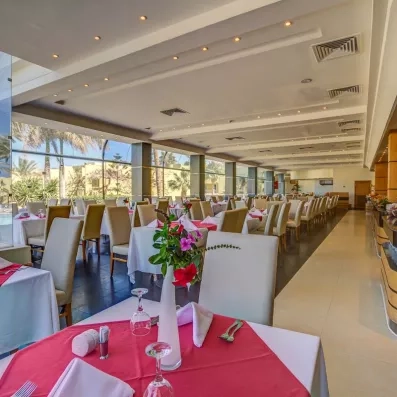 Grande salle de restaurant de l'hôtel, vitre donnant sur le jardin extérieur, tables dressées 