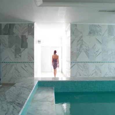 Femme en drap de bain marchant vers un bassin de thalasso en marbre au Royal Thalassa Monastir.
