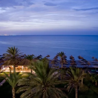 Bar de plage éclairé au crépuscule sous les palmiers face à la mer à l'hôtel Royal Thalassa.