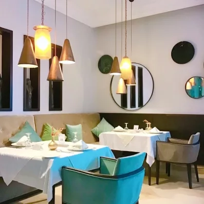 Coin repas intimiste avec fauteuils turquoise et luminaires design au restaurant du Royal Thalassa Monastir.
