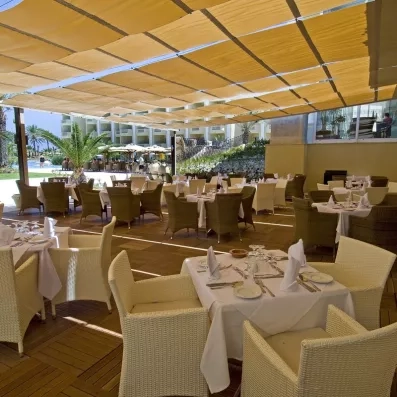 Terrasse de restaurant ombragée avec mobilier en rotin blanc près de la piscine au Royal Thalassa Monastir.